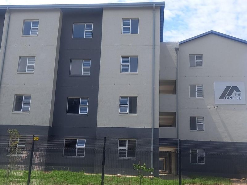 Exterior view of The Bridge apartment complex, featuring a modern multi-story facade with secure perimeter fencing and aluminium window frames.