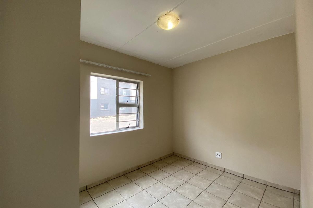 A clean, empty bedroom featuring neutral tiled flooring, a large window with an aluminium frame, and a central ceiling light fixture.
