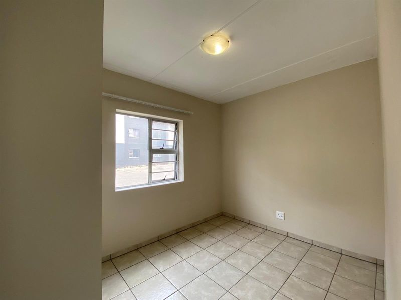 A clean, empty bedroom featuring neutral tiled flooring, a large window with an aluminium frame, and a central ceiling light fixture.