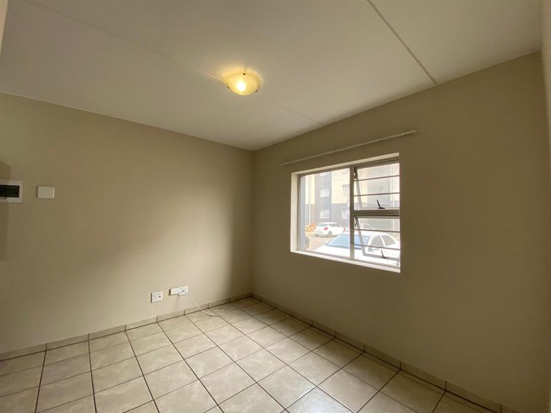 A clean, empty bedroom featuring neutral wall paint, tiled flooring, and a window fitted with security bars.