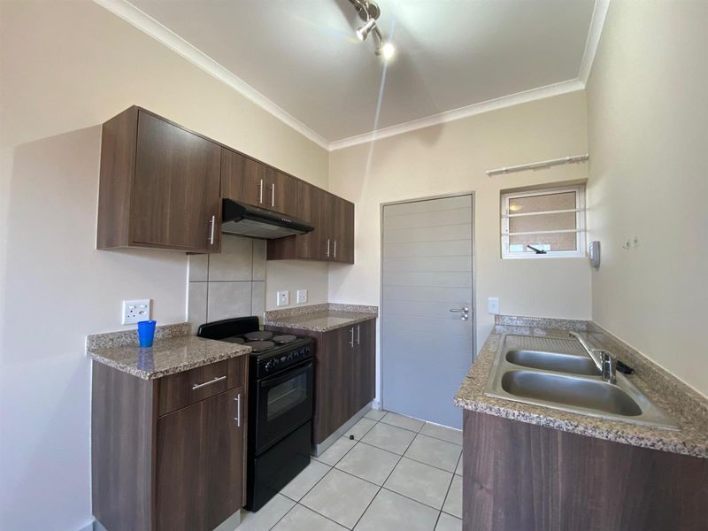 A clean, functional kitchen featuring dark wood-look cabinetry, granite countertops, a double stainless steel sink, and a freestanding electric stove with an extractor fan.