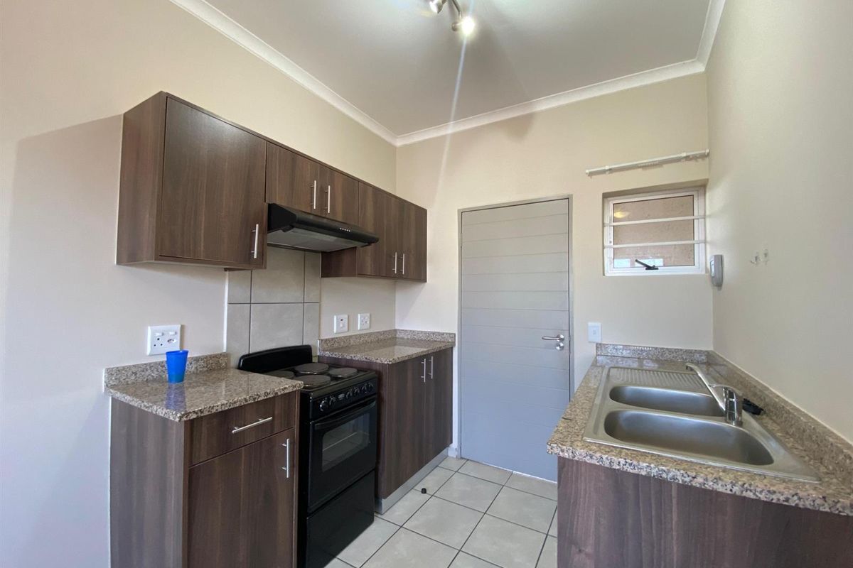 A clean, functional kitchen featuring dark wood-look cabinetry, granite countertops, a double stainless steel sink, and a freestanding electric stove with an extractor fan.