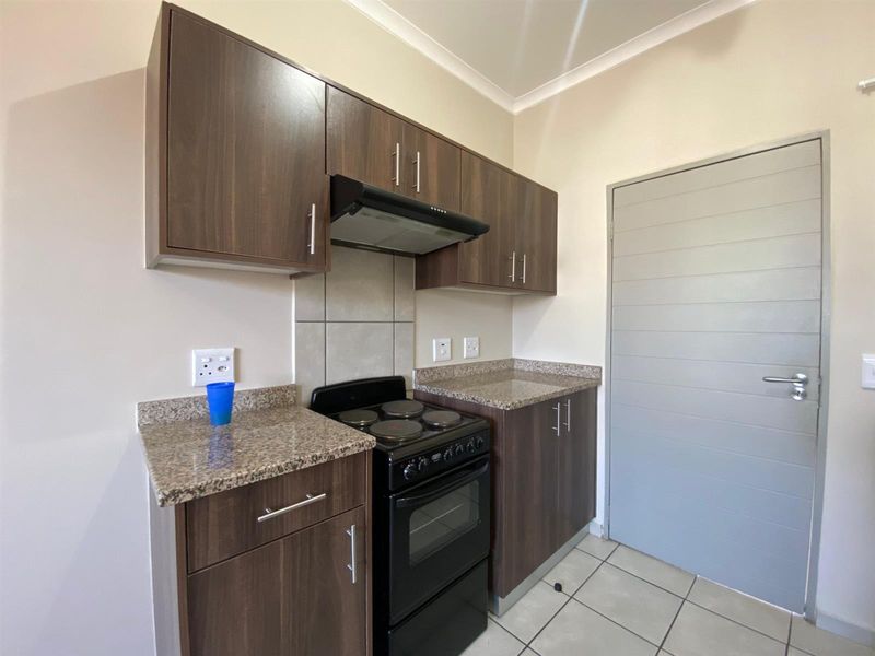 A compact kitchen featuring dark wood-look cabinetry, granite countertops, a built-in electric stove with extractor fan, and neutral tiled flooring.