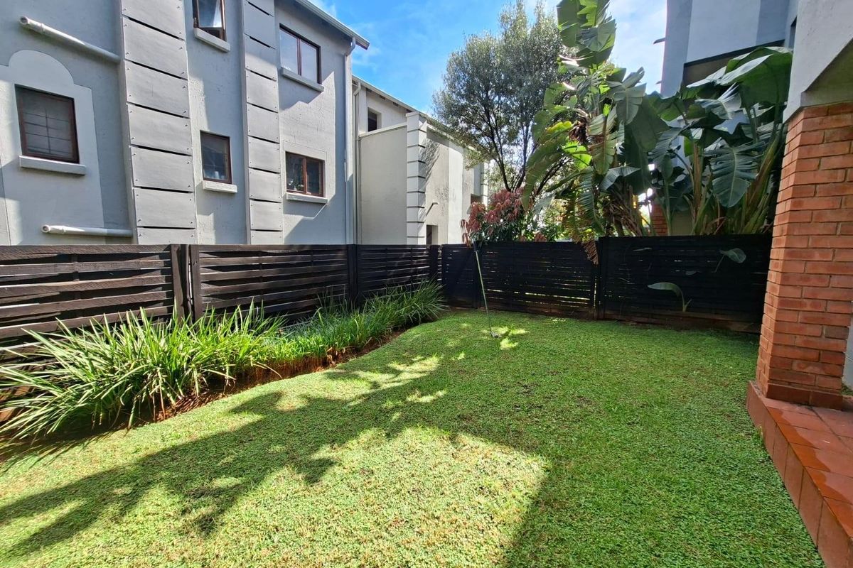 A private rear garden area featuring a well-maintained lawn, perimeter timber fencing, and established garden beds adjacent to the apartment building.