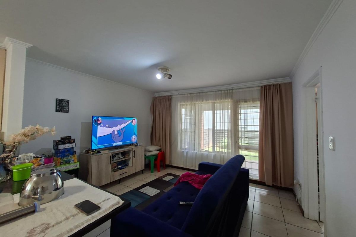 A living room featuring tiled flooring, large windows with curtains, and access to an outdoor area, providing a functional and well-lit living space.