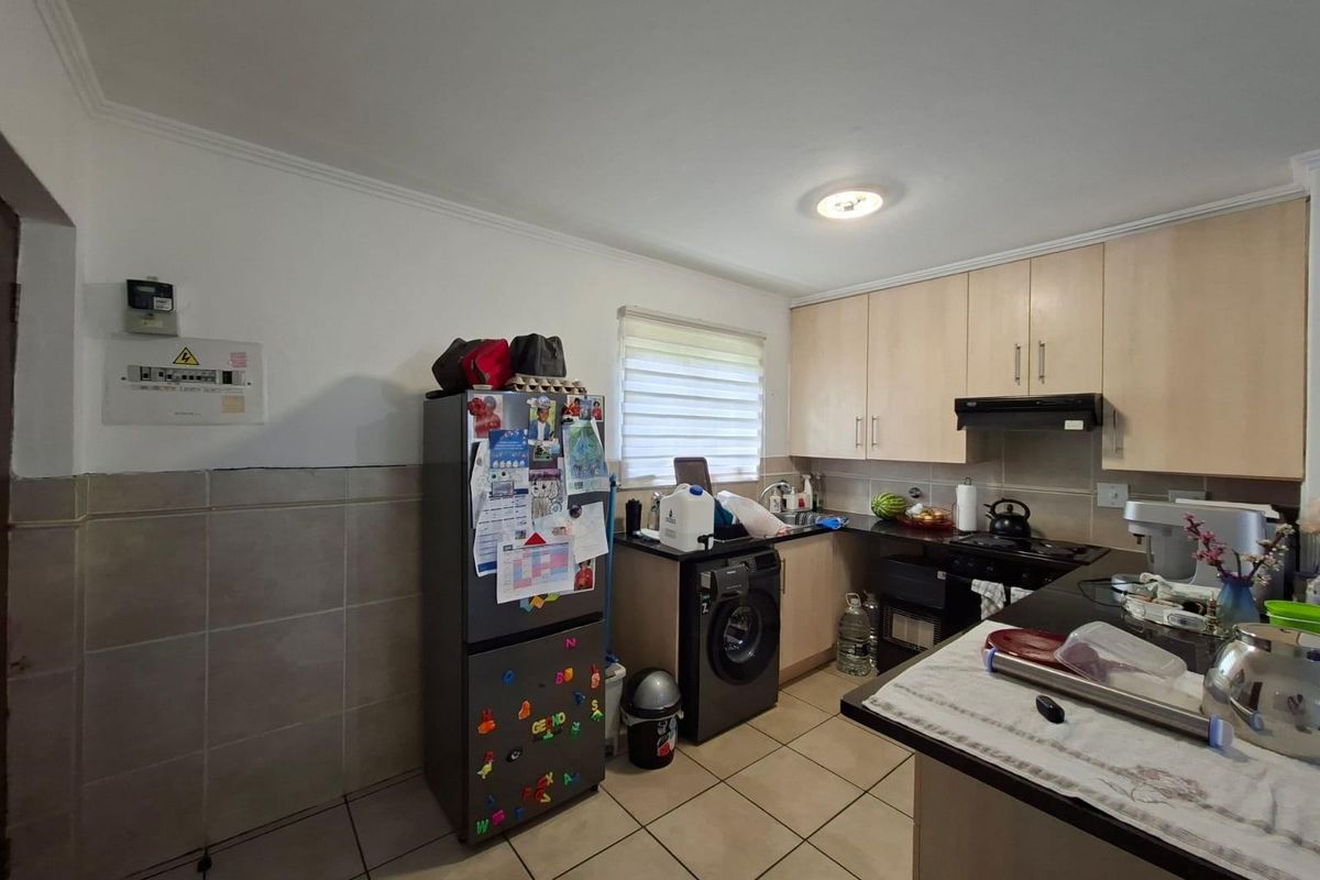 Functional kitchen featuring light wood cabinetry, dark countertops, tiled flooring, and integrated laundry plumbing, offering a practical layout for daily meal preparation.