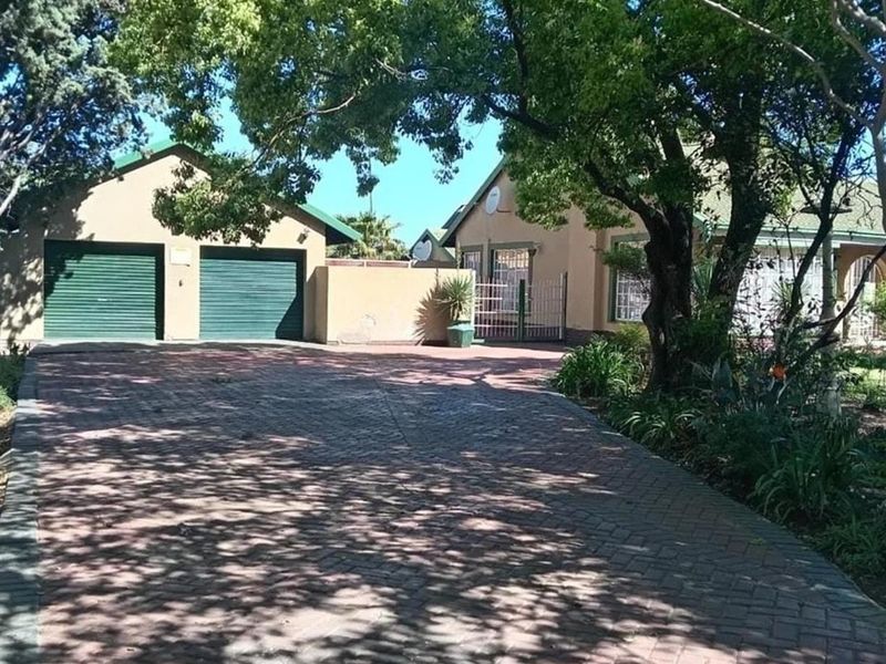 Front view of the property featuring a paved driveway, double garage, and established garden with mature trees.