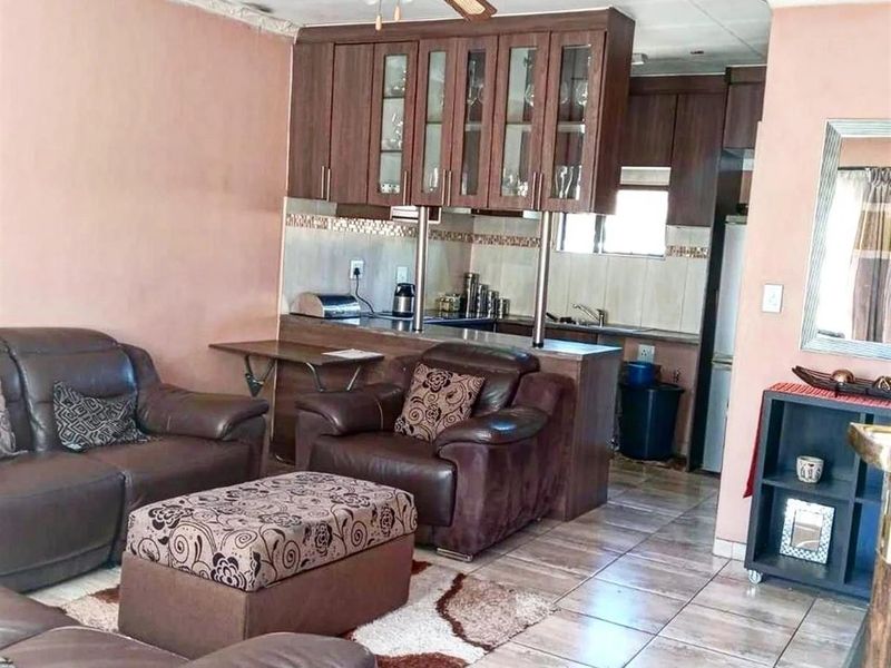 Open-plan living area featuring tiled flooring, a ceiling fan, and a functional kitchen with built-in cabinetry and a breakfast counter.