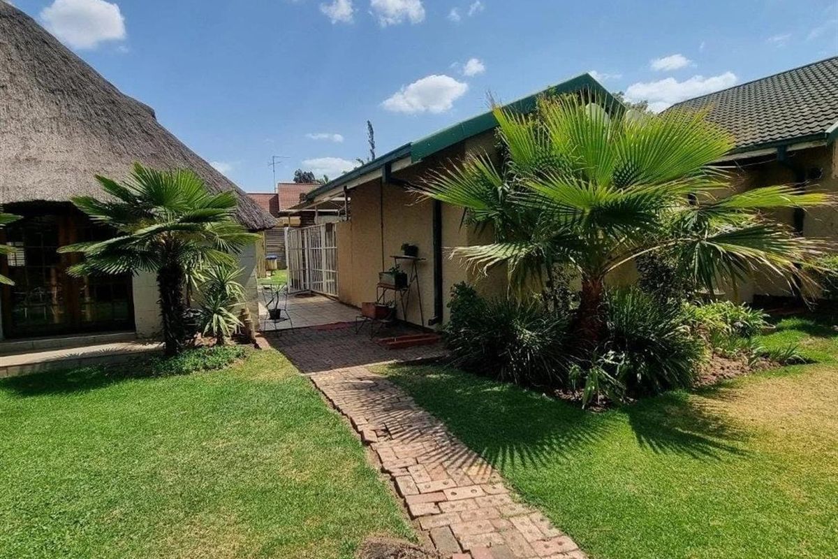 A well-maintained rear garden featuring a brick pathway, lush lawn, and a combination of thatched and tiled roof structures.