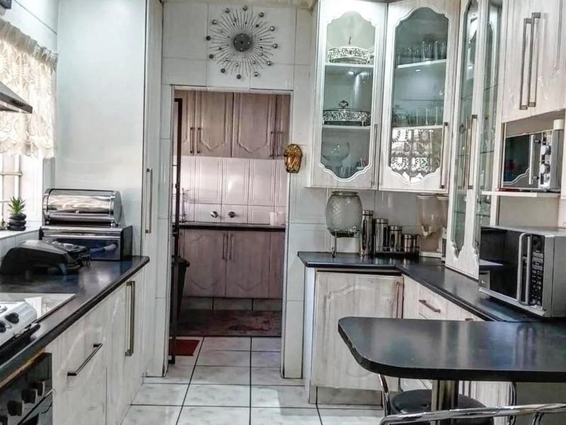 A functional kitchen featuring white cabinetry, dark countertops, and tiled flooring, with an adjoining scullery area providing additional storage and workspace.