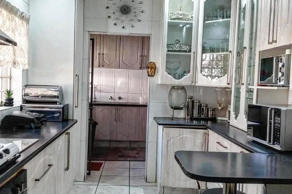 A functional kitchen featuring white cabinetry, dark countertops, and tiled flooring, with an adjoining scullery area providing additional storage and workspace.