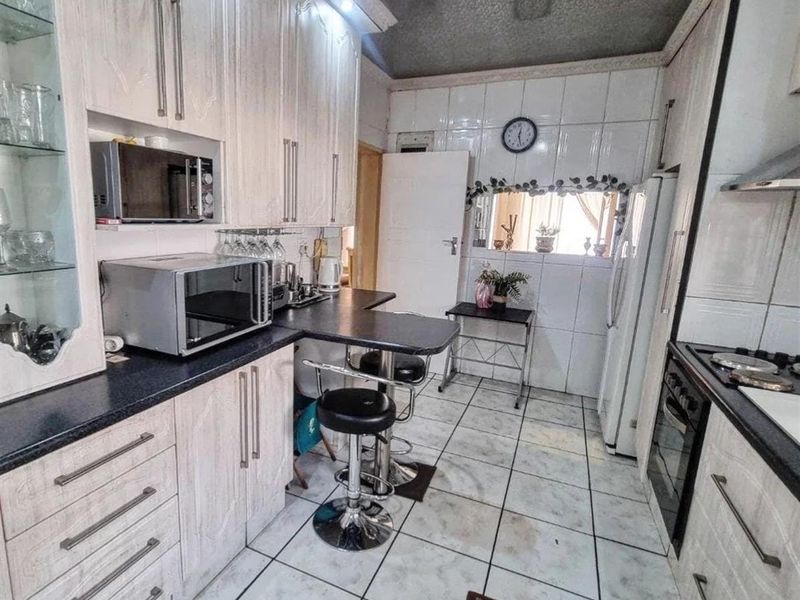 A functional kitchen featuring built-in cabinetry, laminate countertops, a gas hob with extractor, and tiled flooring throughout.