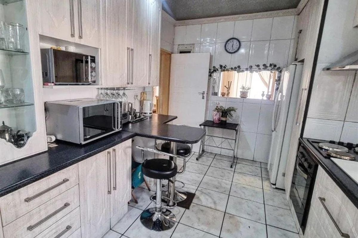 A functional kitchen featuring built-in cabinetry, laminate countertops, a gas hob with extractor, and tiled flooring throughout.