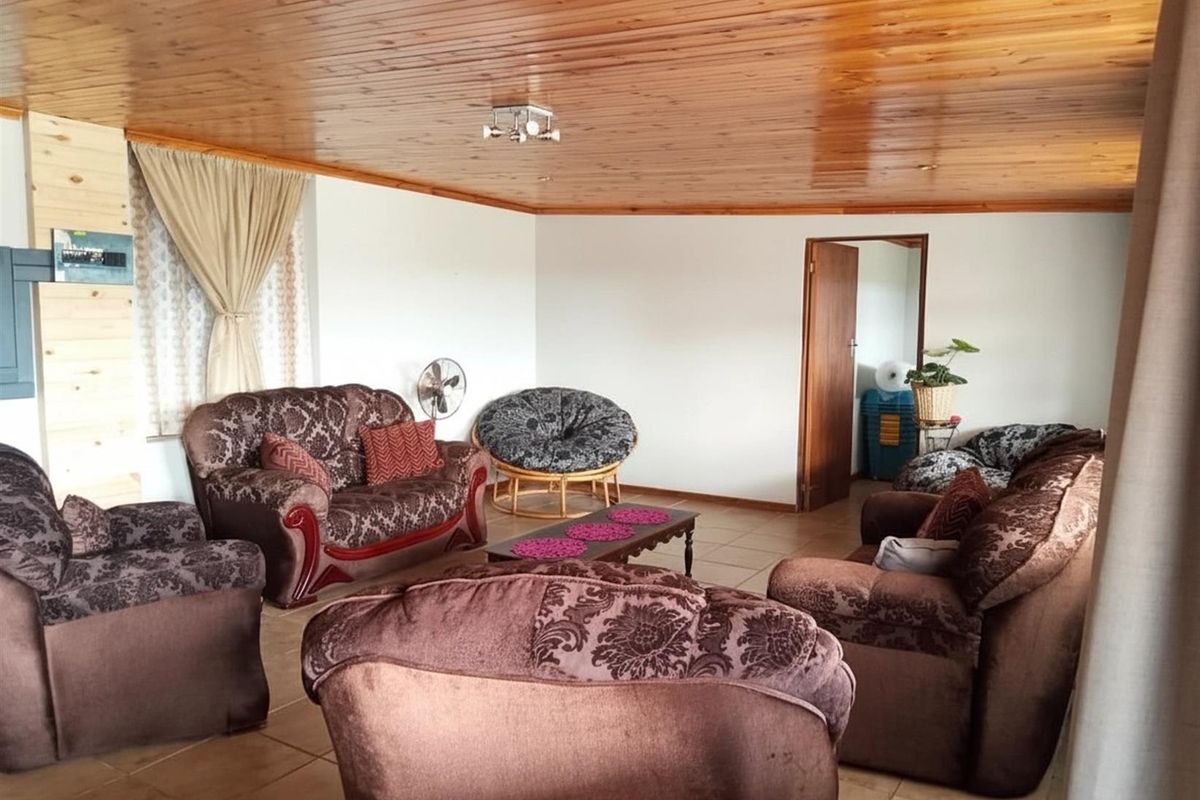 A spacious living room featuring a warm timber-clad ceiling, tiled flooring, and a neutral wall finish, providing a comfortable and functional living area.