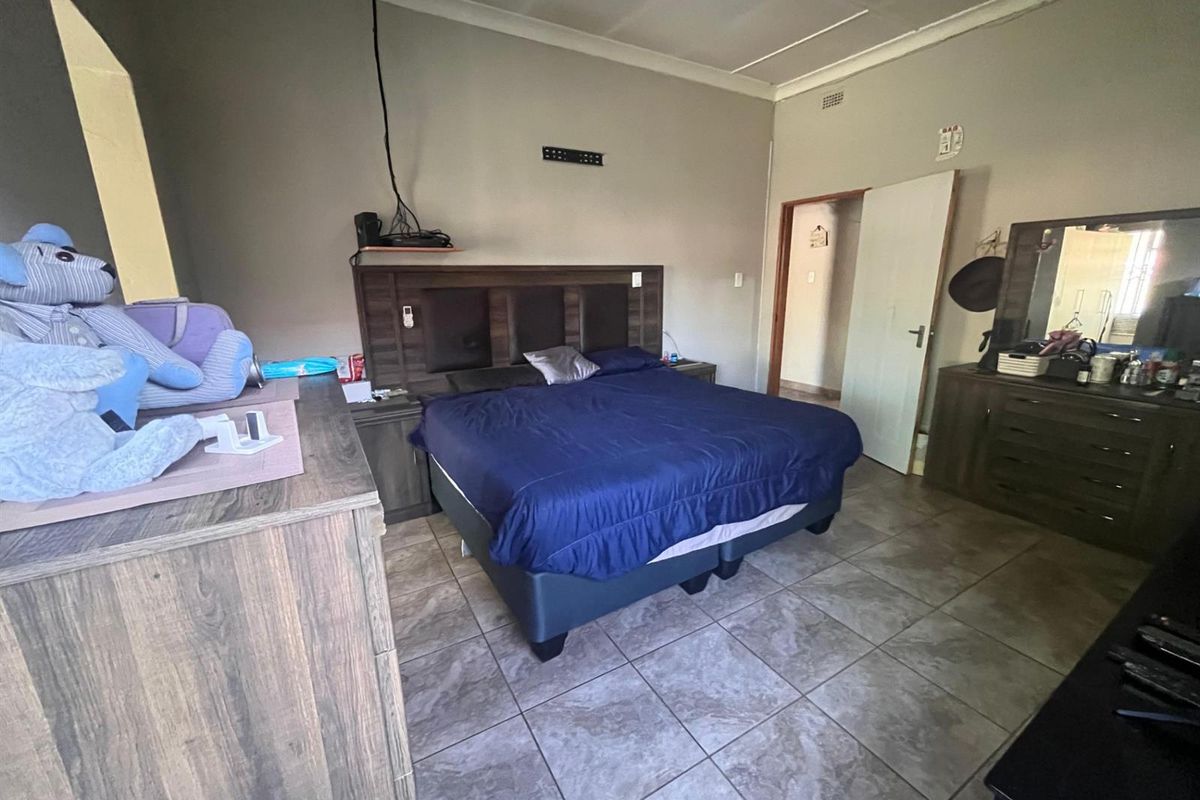 A bedroom featuring tiled flooring, a built-in headboard, and a doorway leading to an adjacent space.