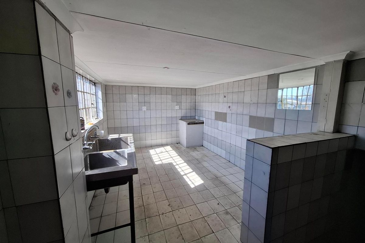 A functional commercial kitchen space featuring tiled walls and flooring, a stainless steel sink unit, and a dedicated prep area.