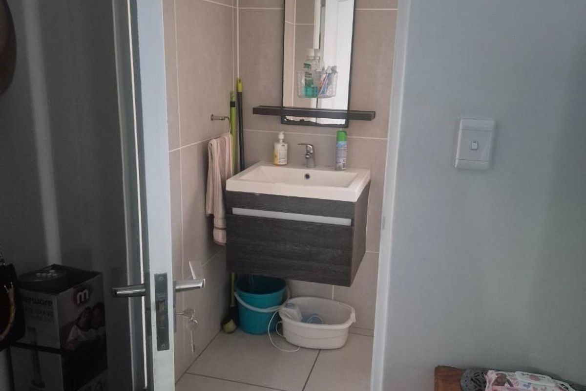 A compact bathroom featuring a wall-mounted vanity with a basin, a mirror, and neutral floor-to-ceiling wall tiling.