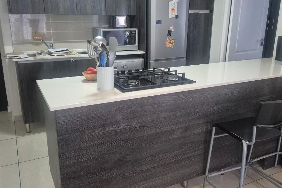 Modern kitchen featuring dark wood-grain cabinetry, a central island with a built-in gas hob, and tiled flooring throughout.