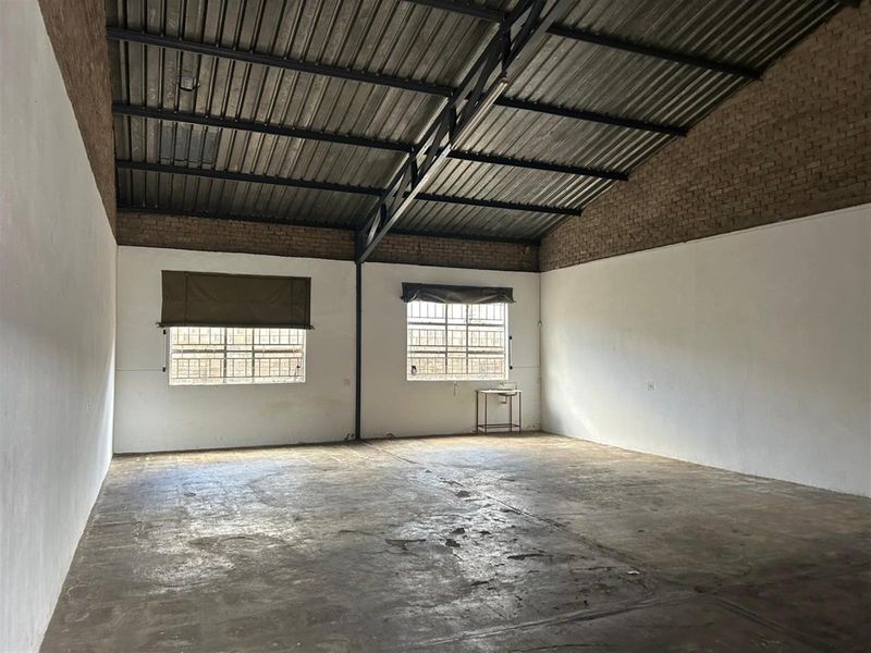 An open-plan commercial space featuring high exposed steel roof trusses, concrete flooring, and large windows providing natural light.