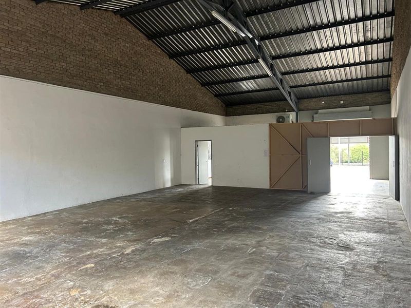 Spacious commercial warehouse unit featuring high exposed ceilings, concrete flooring, and a partitioned office or storage area.