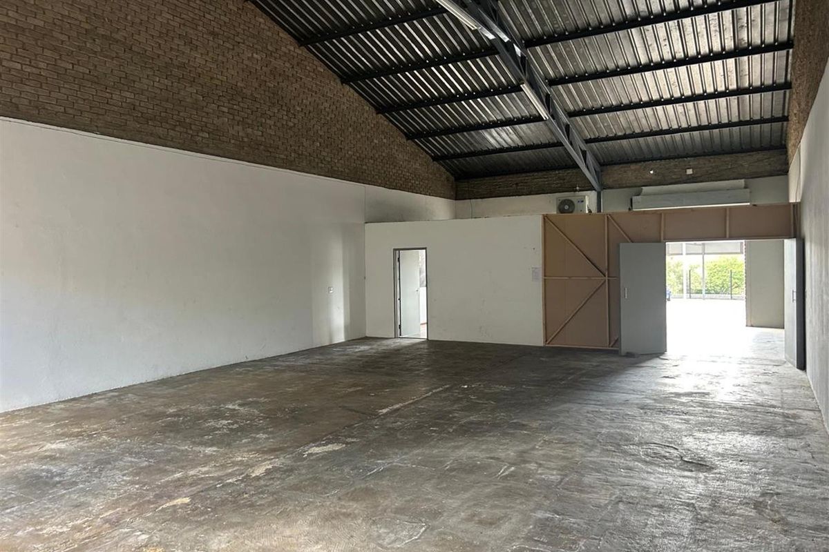 Spacious commercial warehouse unit featuring high exposed ceilings, concrete flooring, and a partitioned office or storage area.