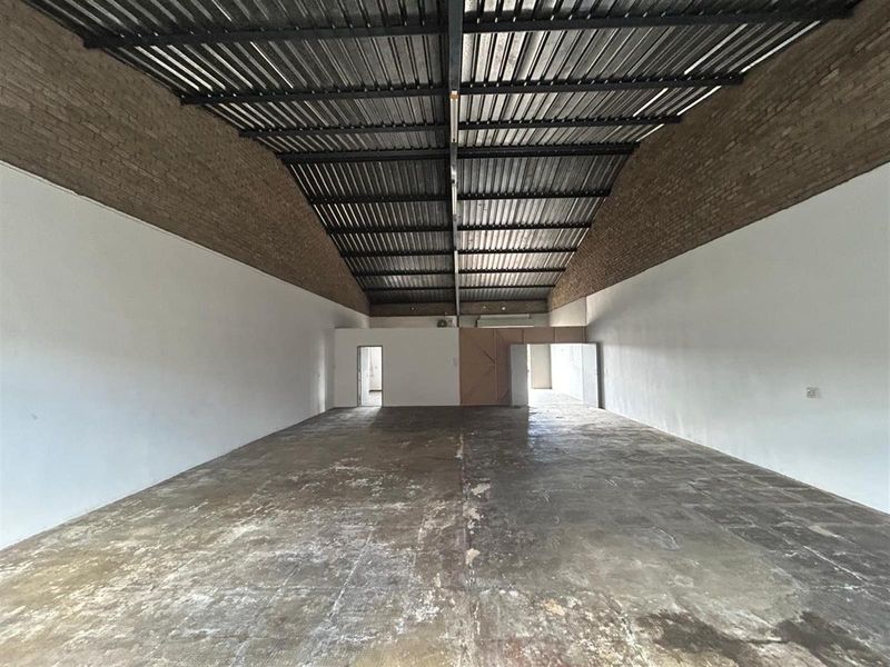 Spacious commercial warehouse or industrial unit featuring high vaulted ceilings, exposed brick walls, and durable concrete flooring, suitable for various business operations.