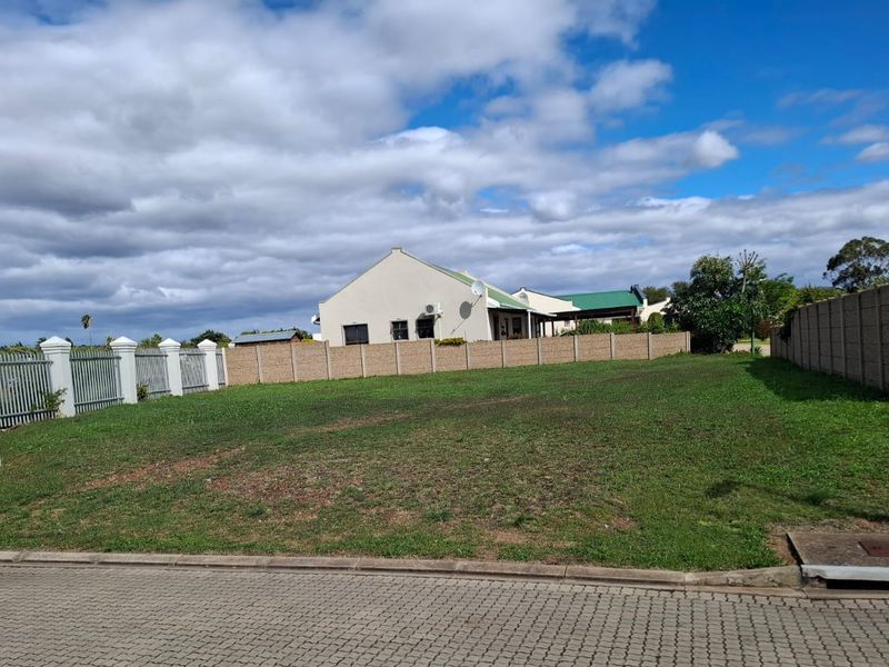 A vacant residential plot featuring a level grassed surface, enclosed by perimeter boundary walls and metal fencing, situated in a developed residential area.