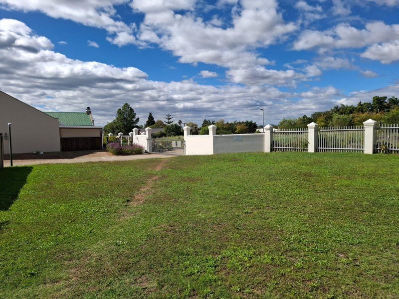 A view of a residential vacant land plot featuring a well-maintained lawn, perimeter walling, and metal fencing.
