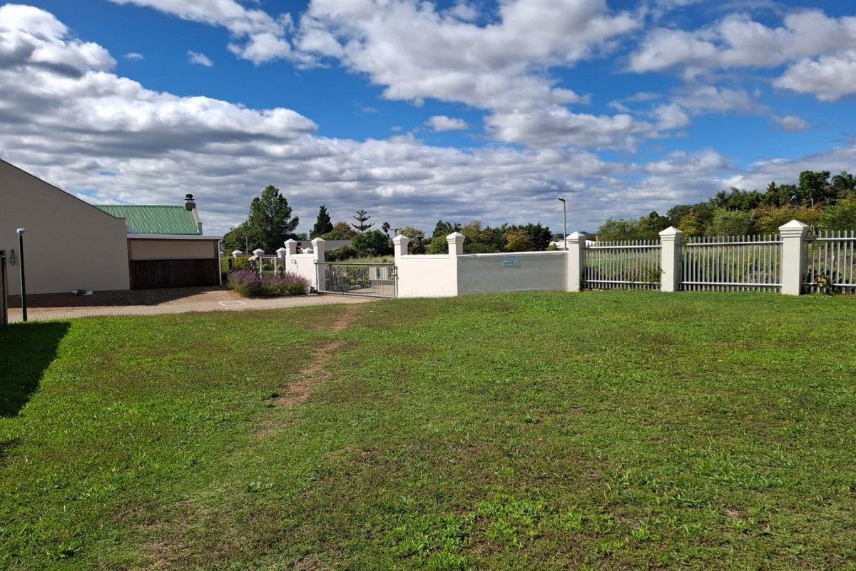 A view of a residential vacant land plot featuring a well-maintained lawn, perimeter walling, and metal fencing.