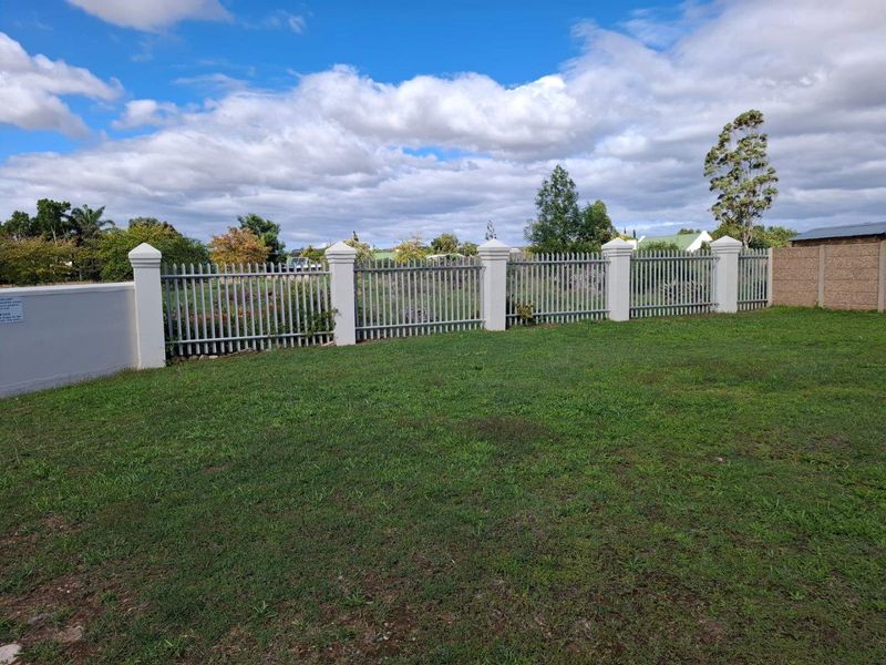 A well-maintained residential plot featuring a manicured lawn and secure perimeter fencing with concrete pillars and metal railings.