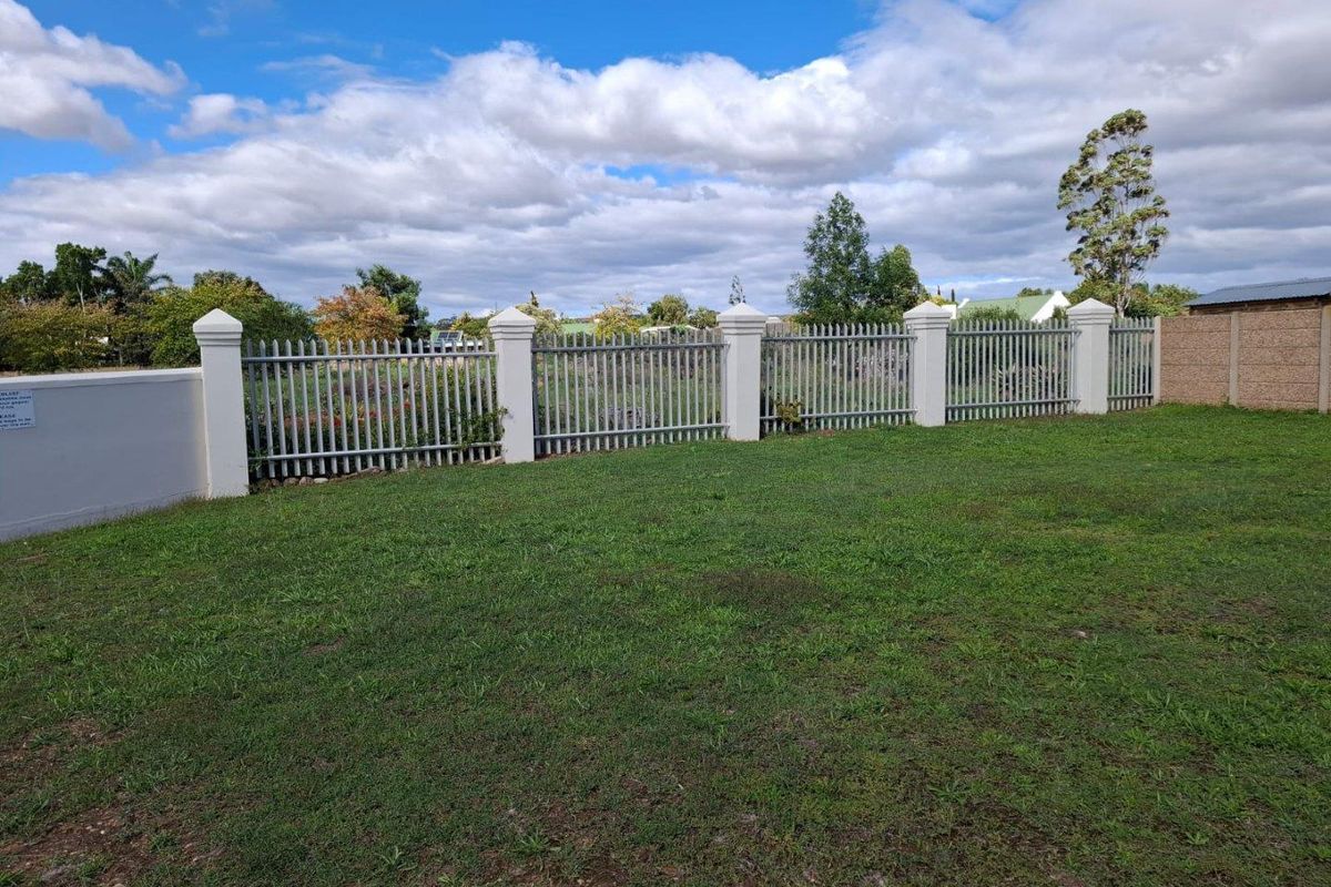 A well-maintained residential plot featuring a manicured lawn and secure perimeter fencing with concrete pillars and metal railings.