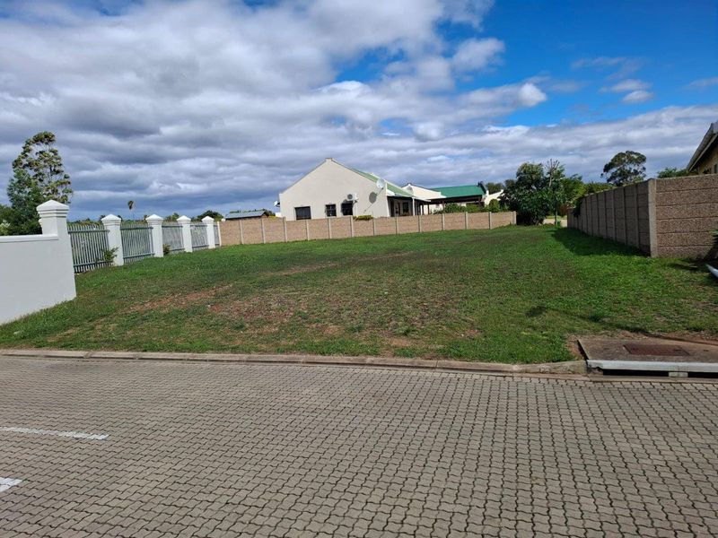 A vacant residential plot featuring established perimeter walling, paved street frontage, and a level grassed surface ready for development.