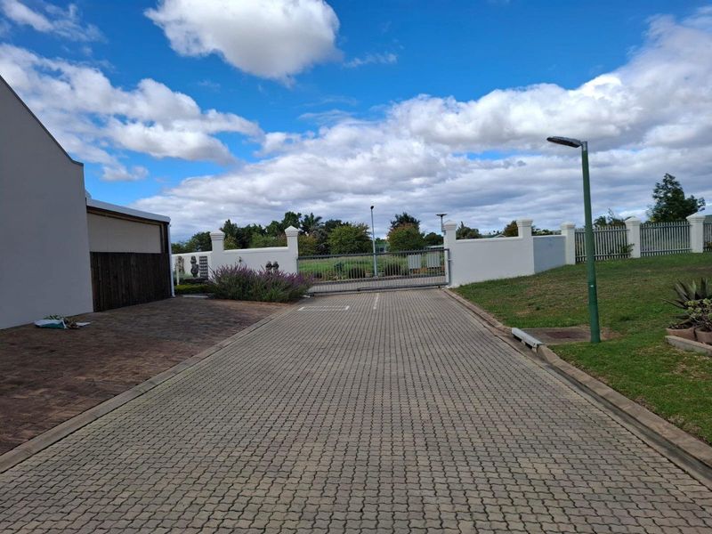 A paved driveway leading to a secure gated entrance with perimeter walling and established landscaping.