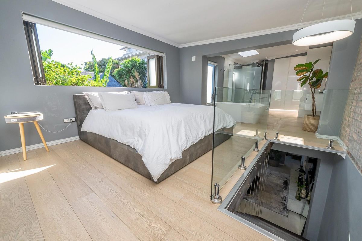 Modern open-plan bedroom featuring light timber flooring, glass balustrades, and an integrated en-suite bathroom with a contemporary soaking tub.