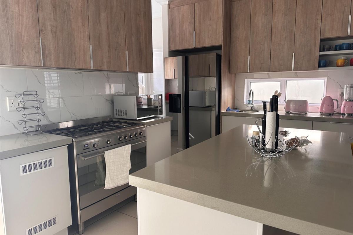 Modern kitchen featuring wood-grain cabinetry, stone countertops, a central island, and a stainless steel gas range with an integrated oven.