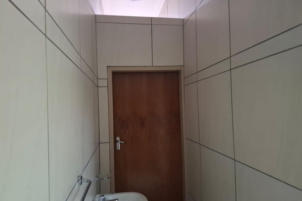 A compact bathroom featuring full-height wall tiling, a built-in basin, and a wooden door.
