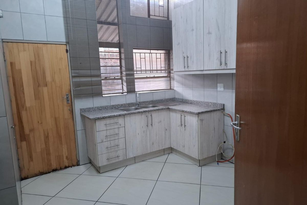 A functional kitchen area featuring light wood-grain cabinetry, granite-look countertops, a double stainless steel sink, and tiled flooring.