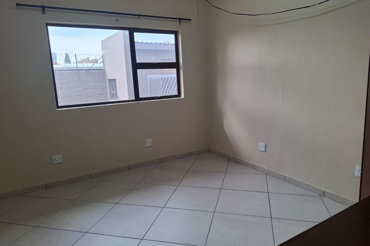 A vacant bedroom featuring neutral tiled flooring, large window with metal frame, and multiple electrical power points.