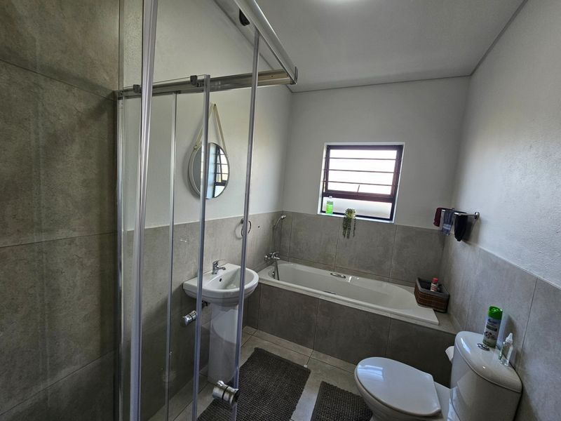 A modern bathroom featuring a tiled bathtub, a separate glass-enclosed shower, a pedestal basin, and a toilet with neutral wall tiling.