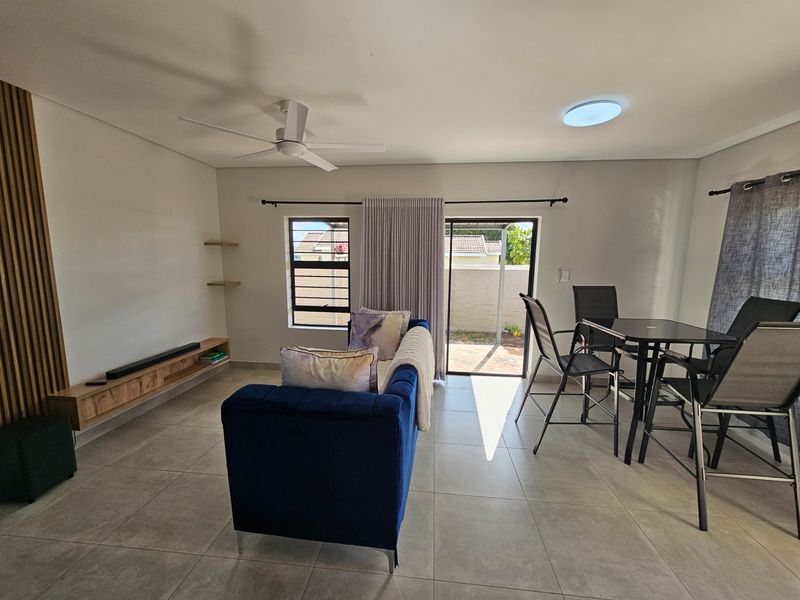 Open-plan living and dining area featuring large format floor tiles, a ceiling fan, and direct access to an outdoor patio space.