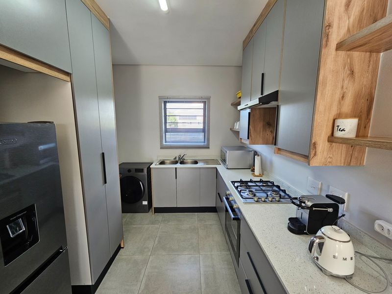 Modern kitchen featuring grey cabinetry, wood-look shelving, stone countertops, a built-in gas hob, oven, and integrated laundry plumbing.