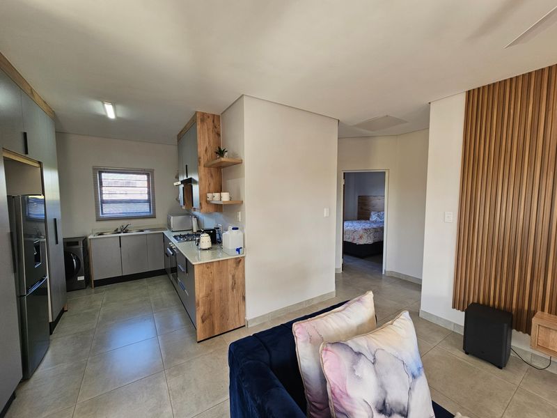 Open plan living area featuring a modern kitchen with wood-look cabinetry, stone countertops, and tiled flooring, leading to a bedroom.