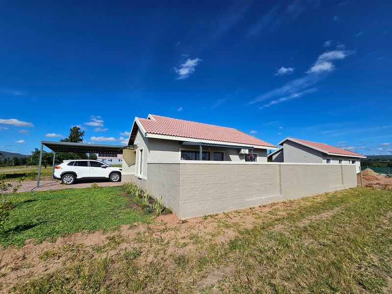 A well-maintained single-story house featuring a tiled roof, a perimeter boundary wall, and a covered carport area.