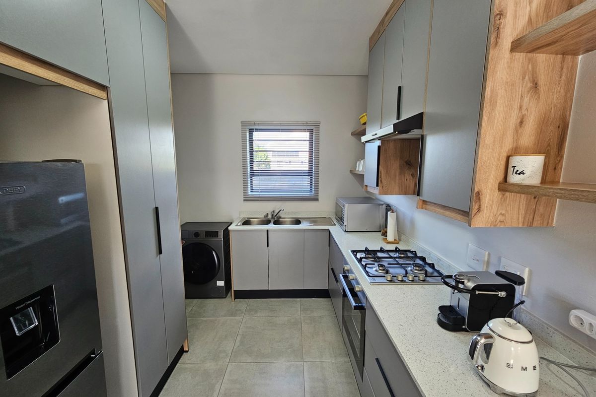 Modern kitchen featuring grey cabinetry, wood-look shelving, stone countertops, a built-in gas hob, oven, and integrated laundry plumbing.