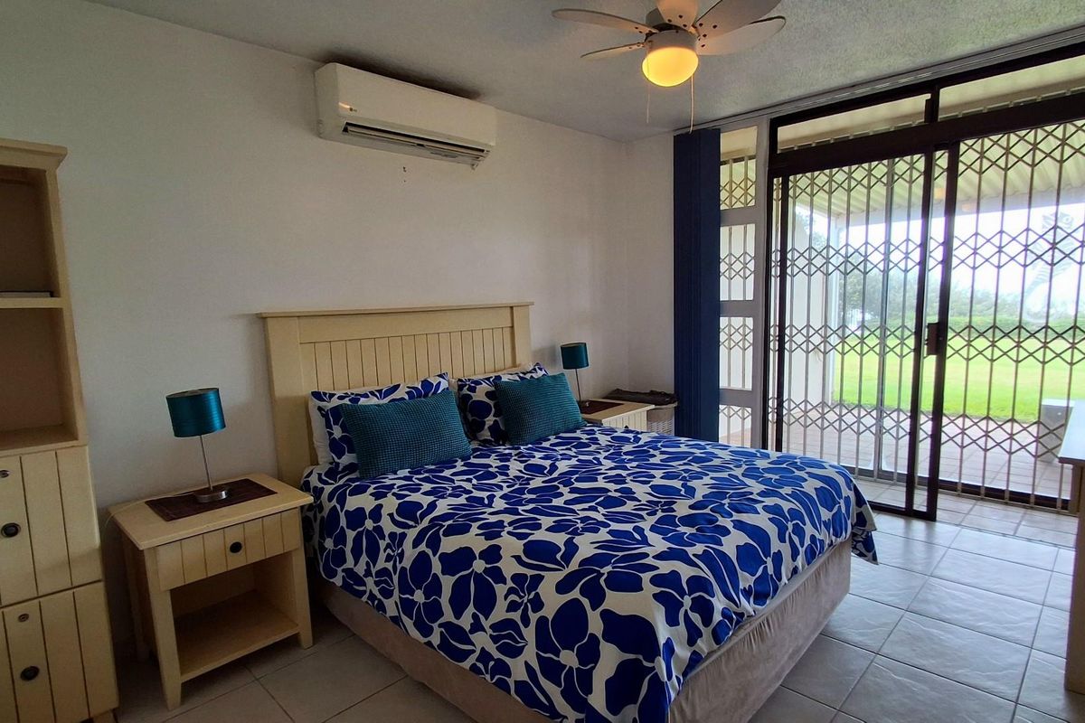 A bedroom featuring tiled flooring, a wall-mounted air conditioning unit, a ceiling fan, and sliding glass doors with security gates leading to the outdoors.