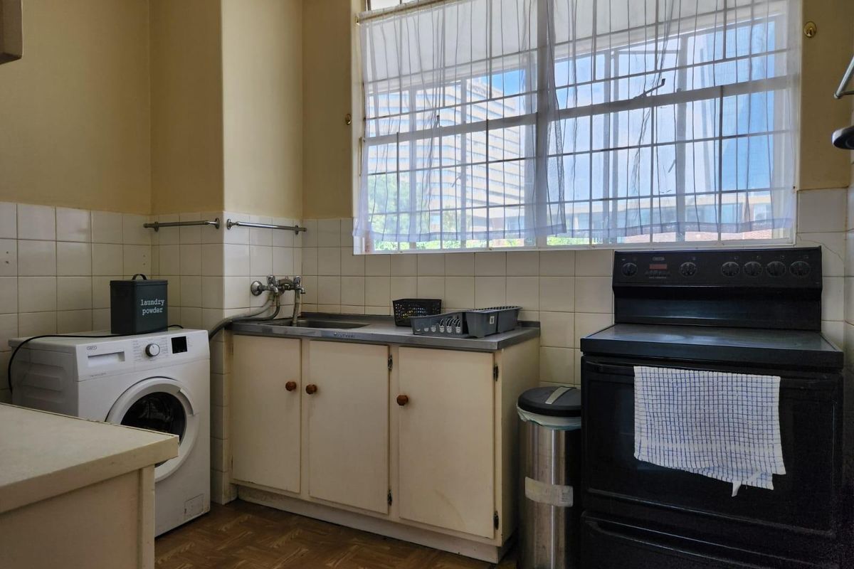 A functional kitchen and laundry area featuring built-in cabinetry, a stainless steel sink, and space for a washing machine and freestanding stove.