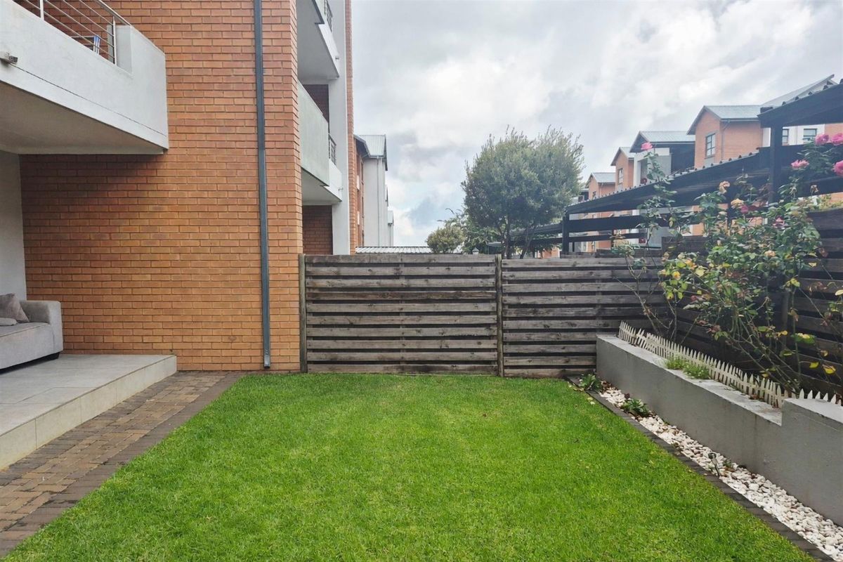 A private rear garden featuring a manicured lawn, paved border, and timber boundary fencing, adjacent to the townhouse brick facade.