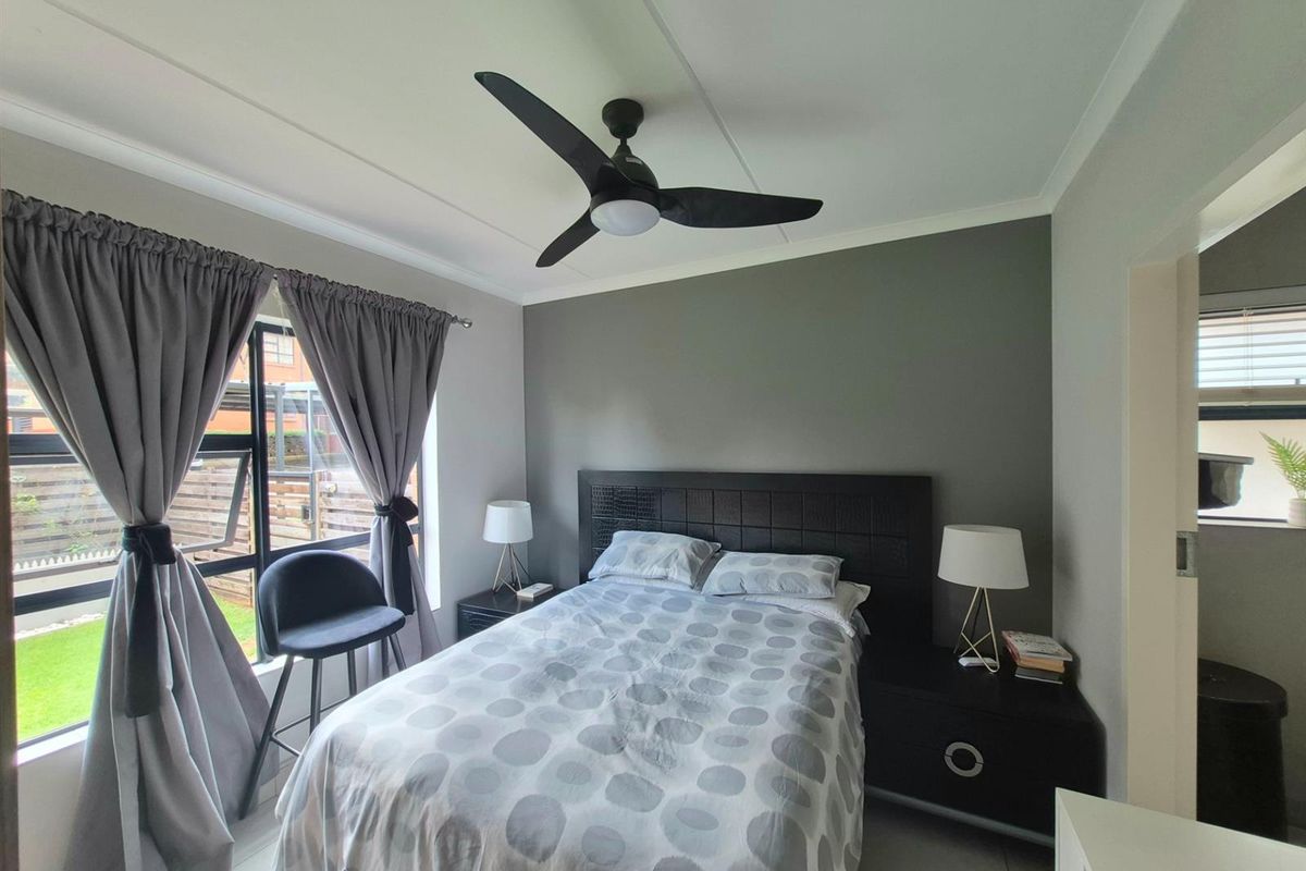 A well-maintained bedroom featuring a ceiling fan, tiled flooring, and a large window allowing natural light.