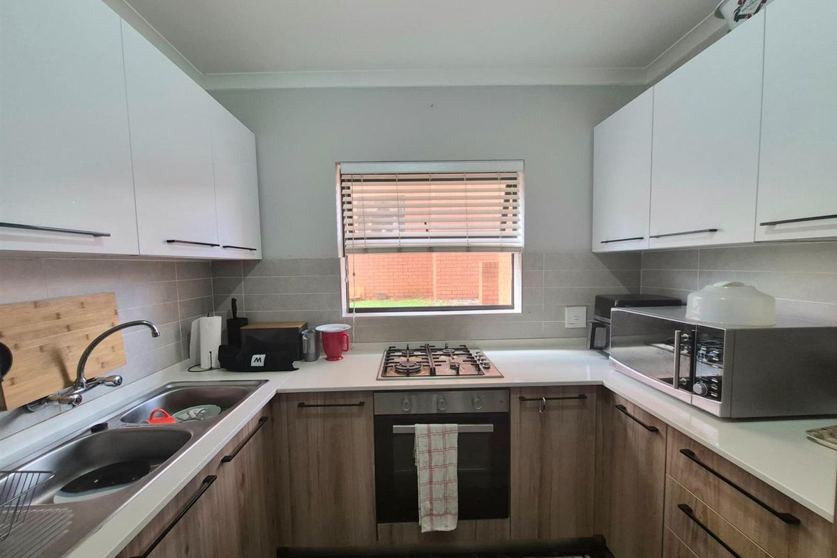 A modern U-shaped kitchen featuring light wood-grain lower cabinetry, white upper cabinets, stone-look countertops, a built-in oven, gas hob, and a double stainless steel sink.