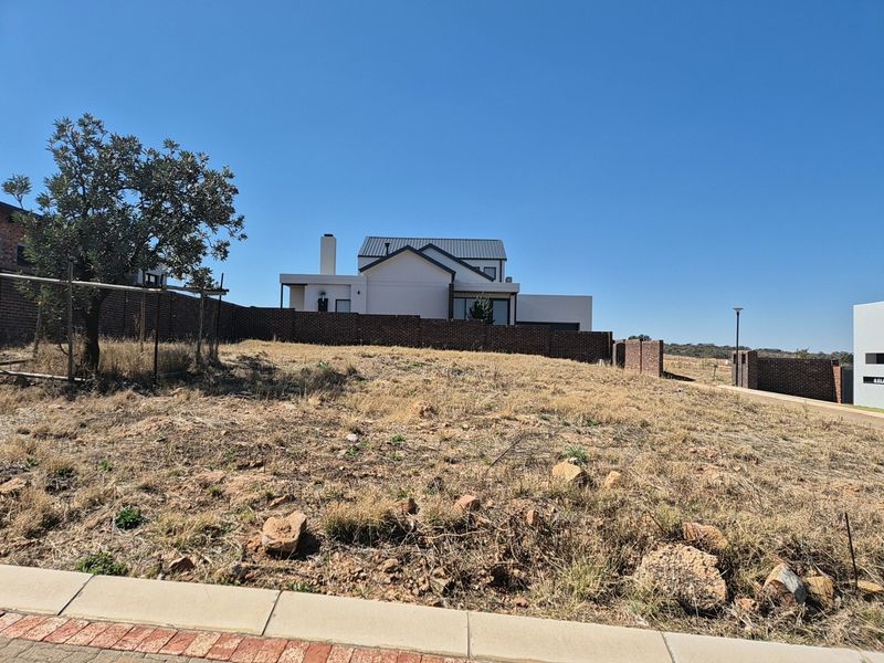 A vacant residential plot featuring a brick boundary wall and street-level access, situated in a developed neighborhood setting.